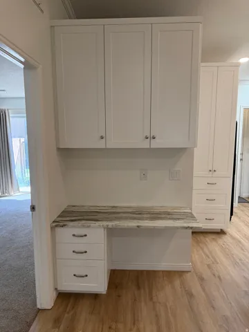 Built-in desk with a stone-finish countertop, white cabinetry with silver hardware, and wood-finish flooring