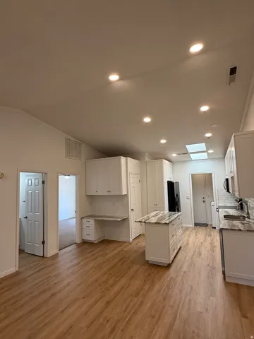 Vaulted ceiling with recessed lighting and skylight, wood-finish flooring, white cabinetry, integrated desk space, and a kitchen island with stone countertop