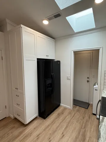 White shaker cabinetry with crown molding, wood-finish flooring, recessed lighting, and a skylight