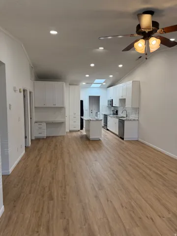 Vaulted ceilings, wood-finish flooring, recessed lighting, white shaker-style cabinetry, and a kitchen island with stone countertops