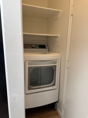 Laundry closet featuring a stacked white dryer unit and built-in shelving