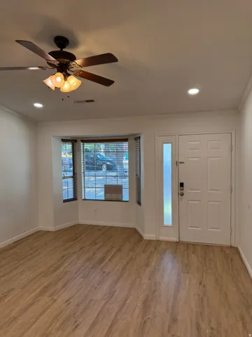 Wood-finish flooring throughout, bay window with blinds, ceiling fan, recessed lighting, and a paneled entry door with a frosted glass side panel