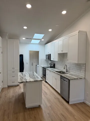 Kitchen featuring vaulted ceilings with recessed lighting and two skylights, white shaker-style cabinetry, granite countertops, and wood-finish flooring