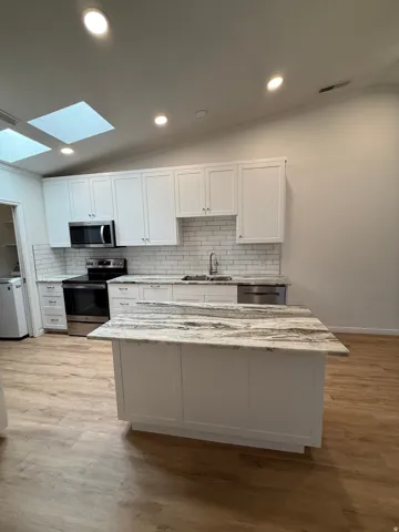Kitchen featuring white cabinetry, stainless steel appliances, a subway tile backsplash, a center island with a stone countertop, and wood-finish flooring