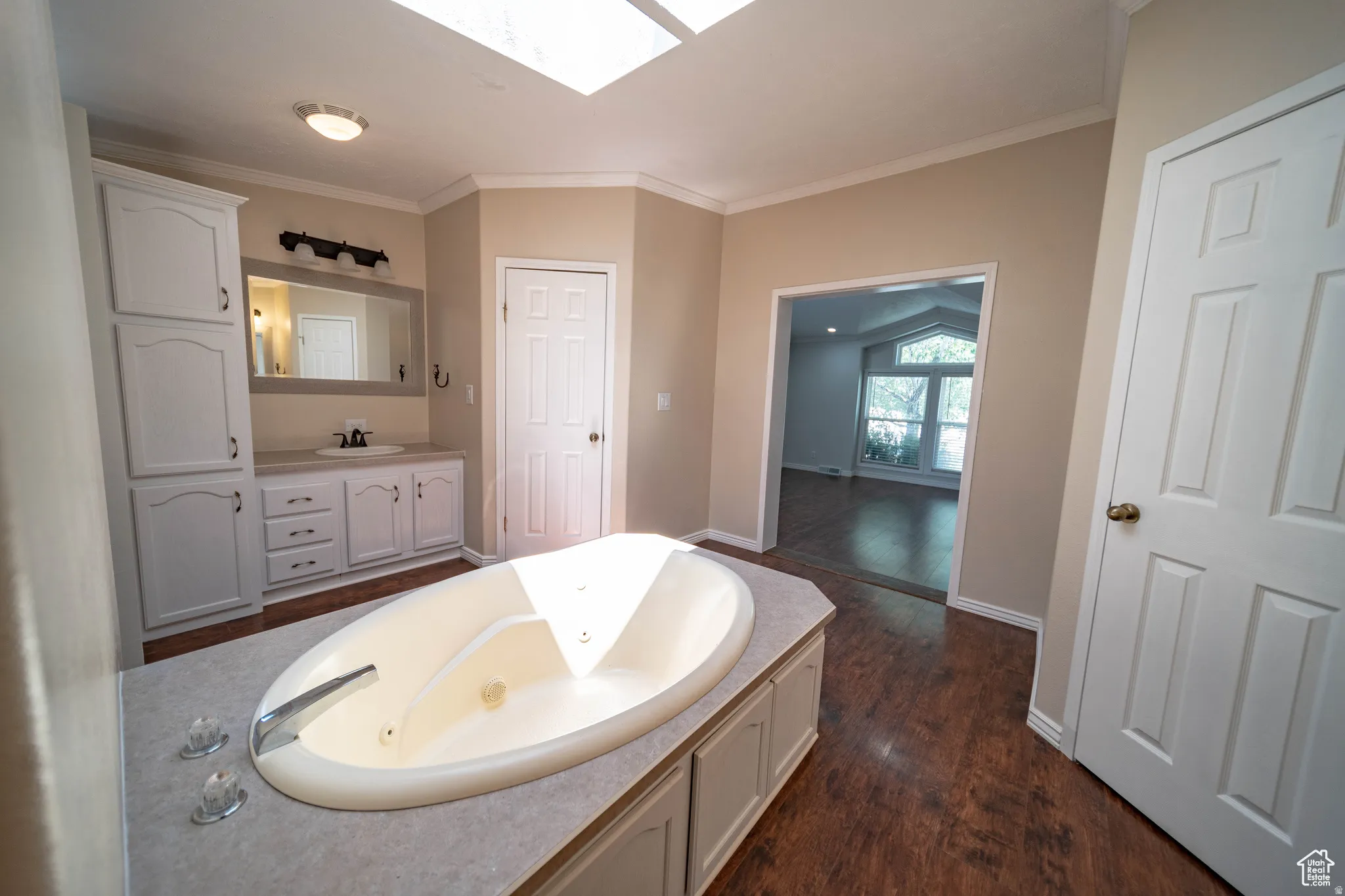 Full Master Bathroom featuring a skylight, a jetted tub, crown molding, vanity, and dark wood-style floors