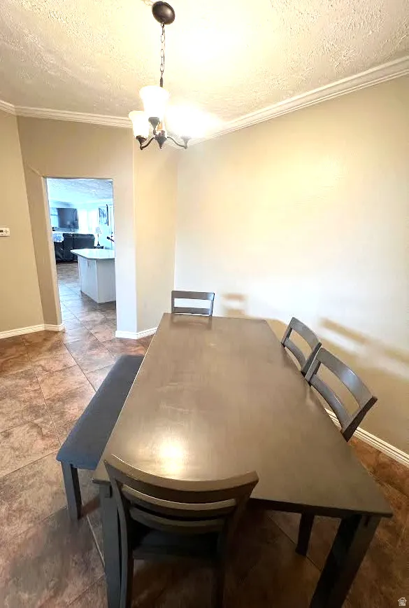 Dining area featuring a textured ceiling, ornamental molding, and hanging lights