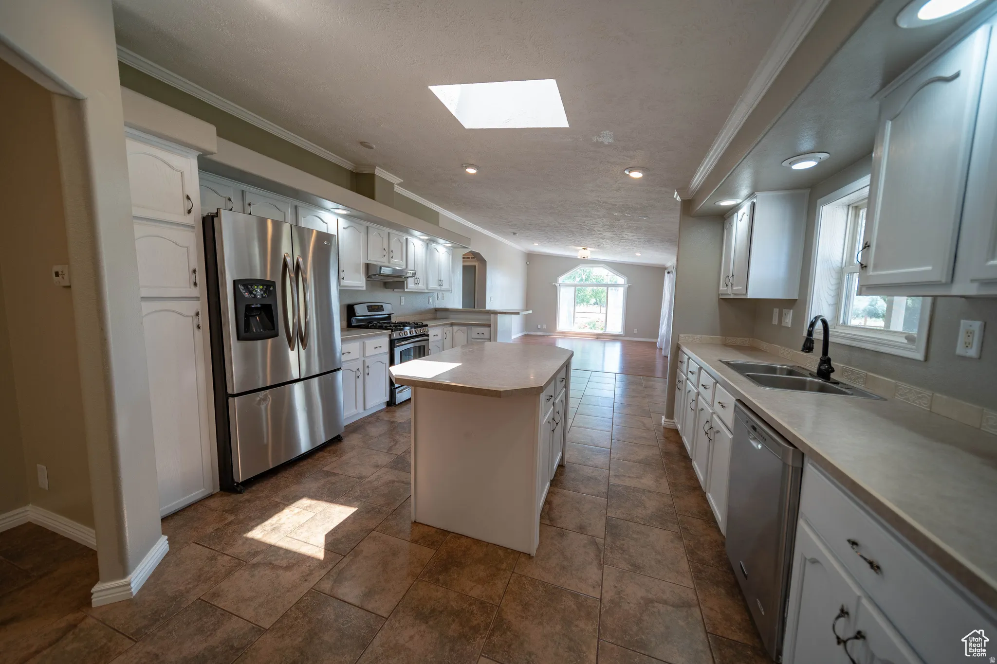 Kitchen with stainless steel appliances, a center island, a skylight, crown molding, and white cabinetry