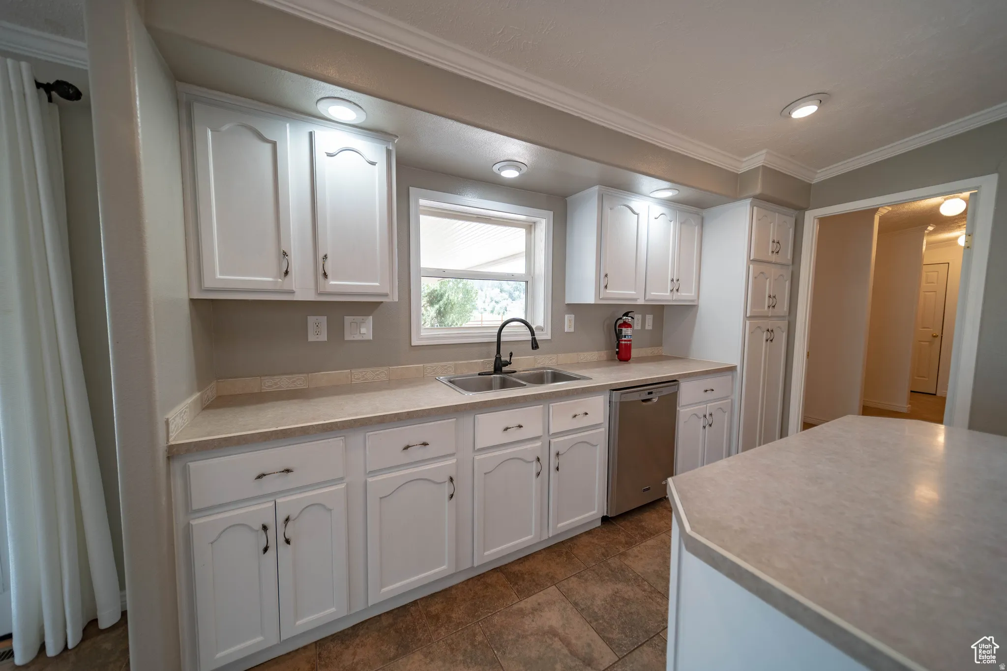 Kitchen featuring white cabinets, crown molding, light countertops, and dishwasher