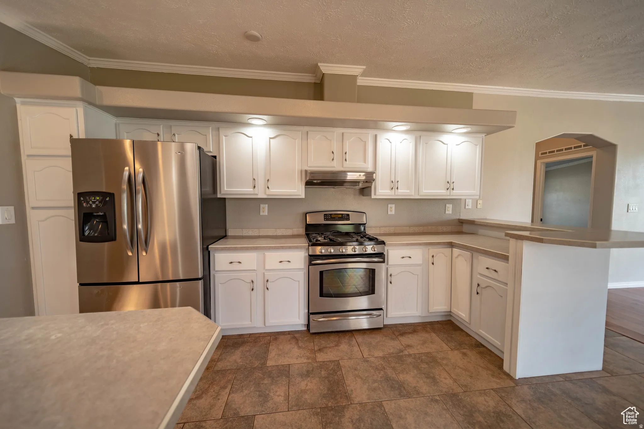 Kitchen featuring a peninsula, stainless steel appliances, white cabinets, ornamental molding, and light countertops
