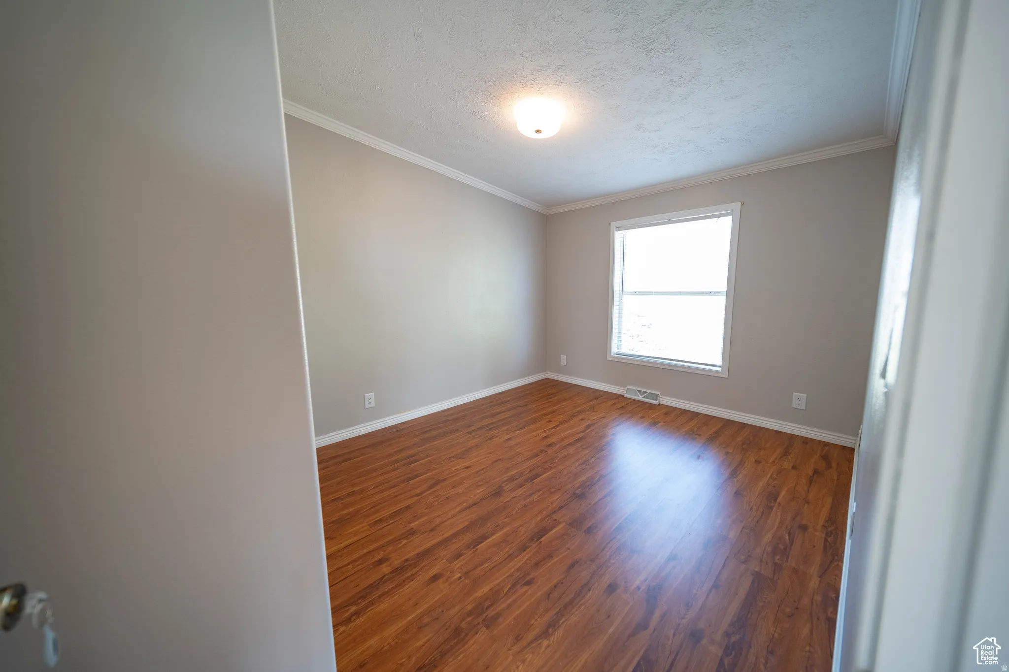 Bedroom 1 with dark wood-style floors, a textured ceiling, and ornamental molding