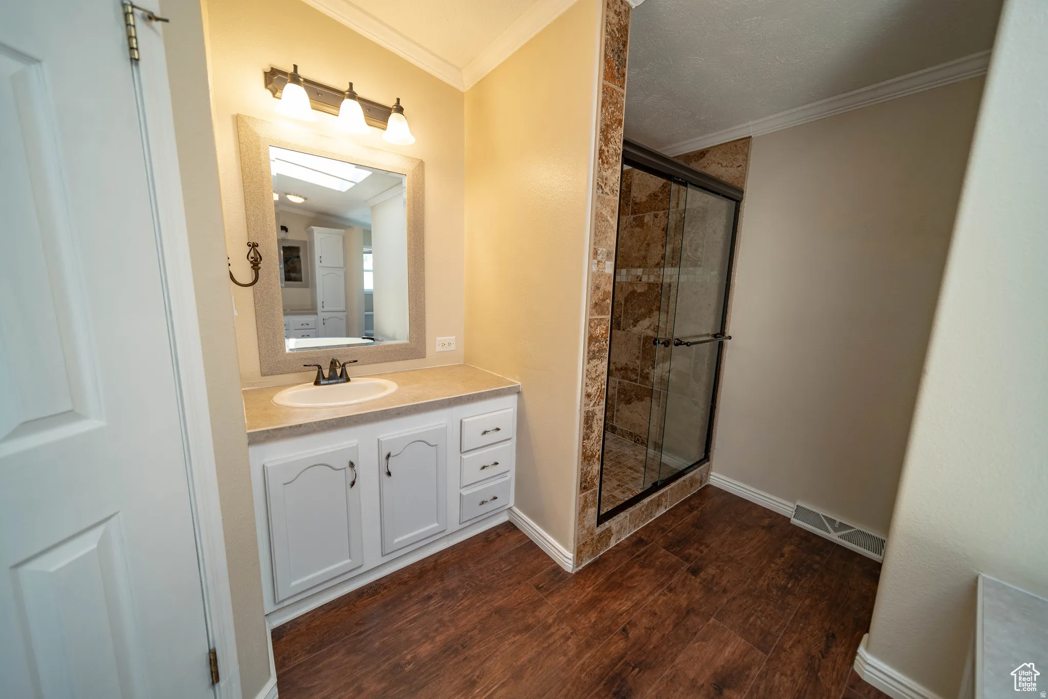 Full Mater Bathroom with vanity, a stall shower, ornamental molding, and dark wood-style floors