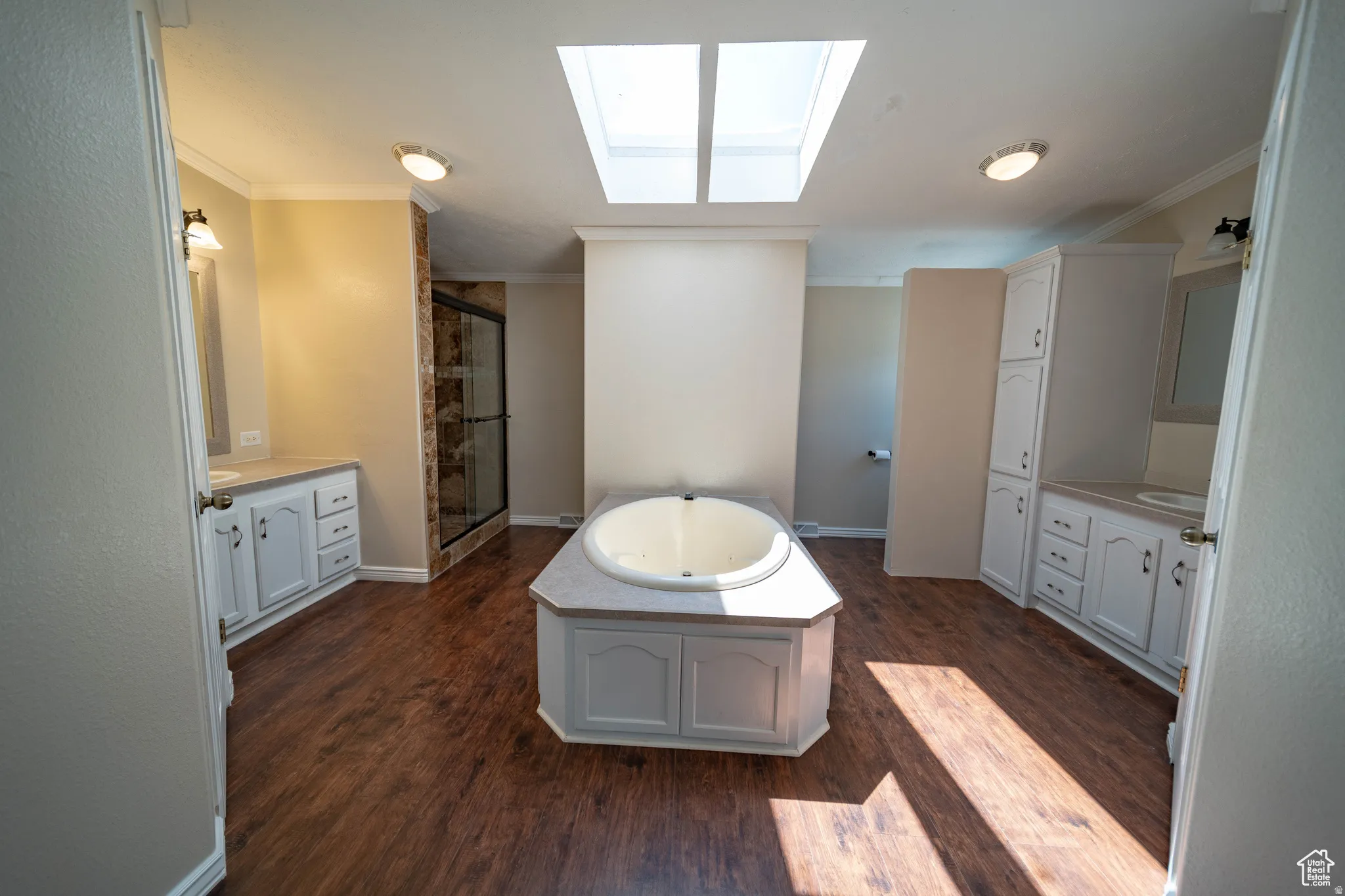 Full Master bath featuring a skylight, ornamental molding, a jetted tub, dark wood-type flooring, and a shower stall