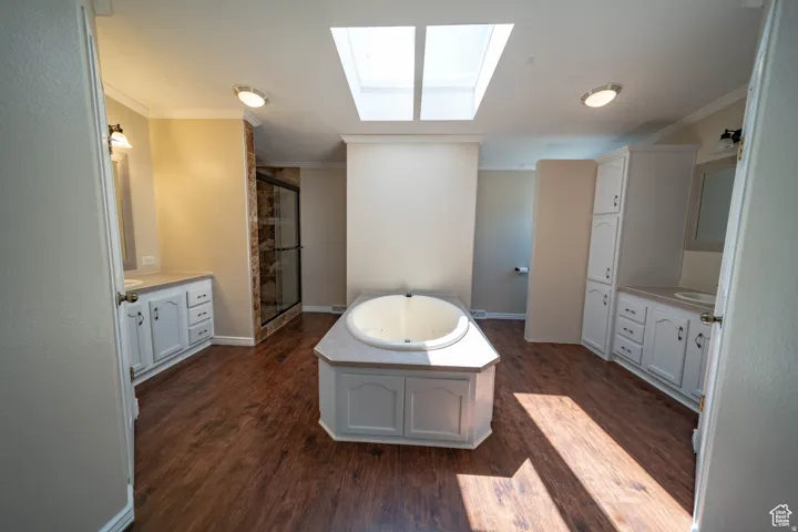 Full Master bath featuring a skylight, ornamental molding, a jetted tub, dark wood-type flooring, and a shower stall