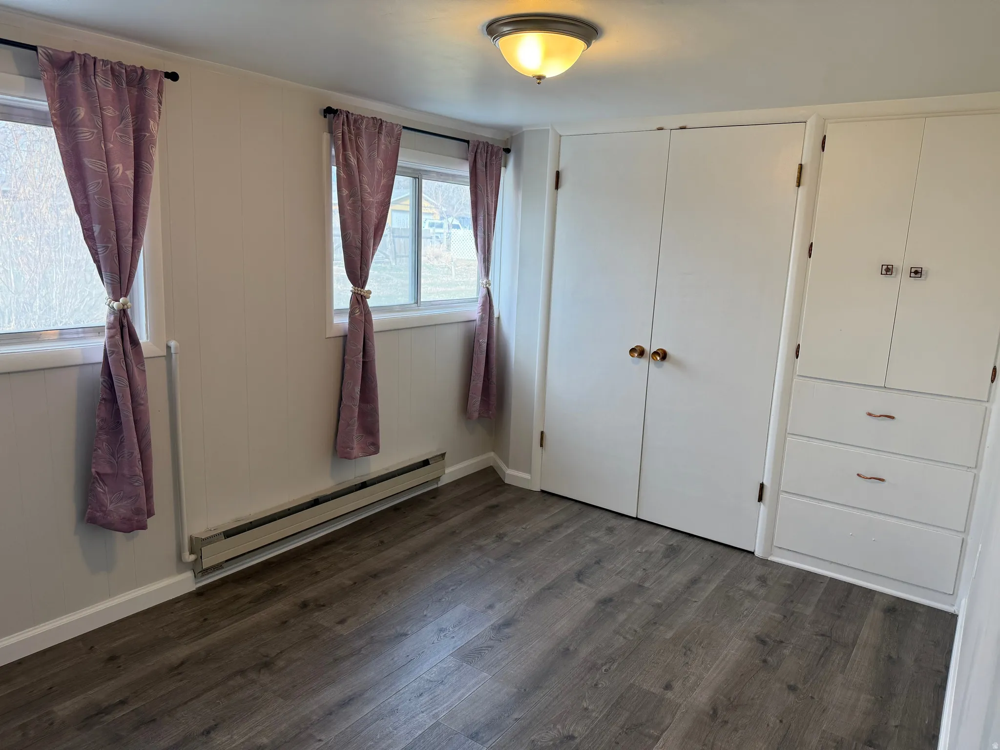 Unfurnished bedroom with a baseboard heating unit, dark wood-style flooring, and a closet