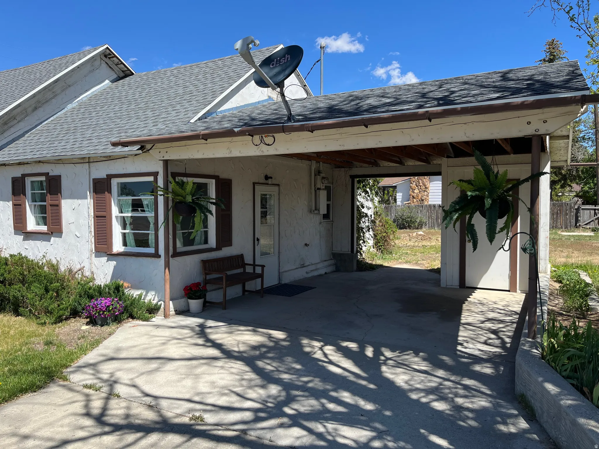 Covered carport with concrete flooring, stucco exterior, and multi-pane windows with decorative shutters
