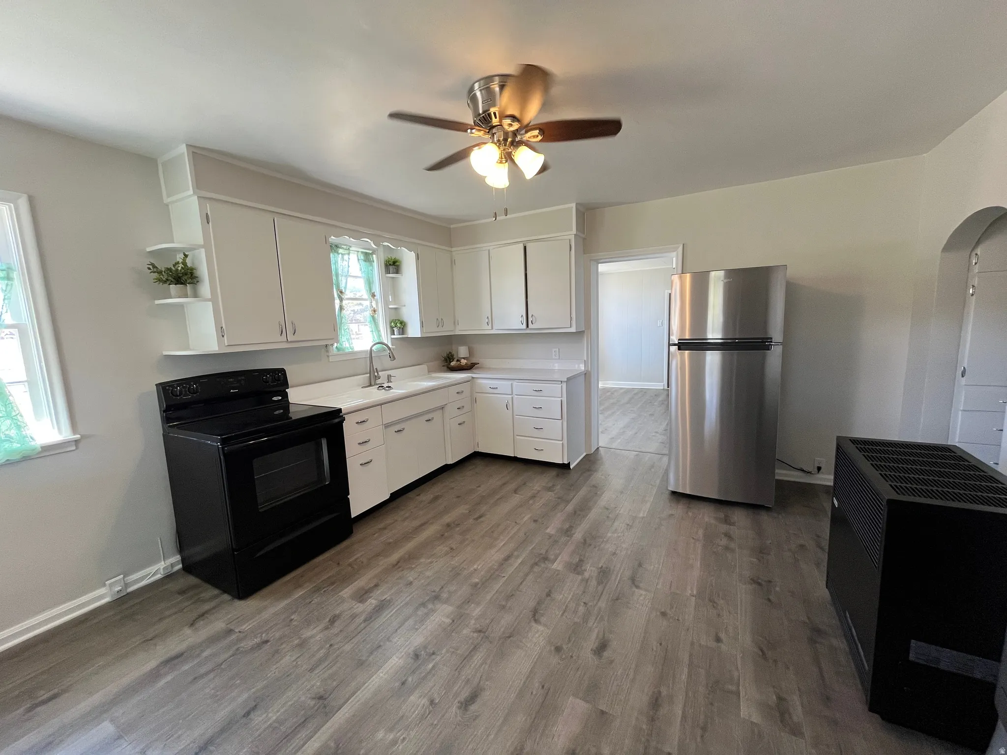 Kitchen featuring white cabinetry, light-toned countertops, a stainless steel refrigerator, black electric range, and wood-finish flooring