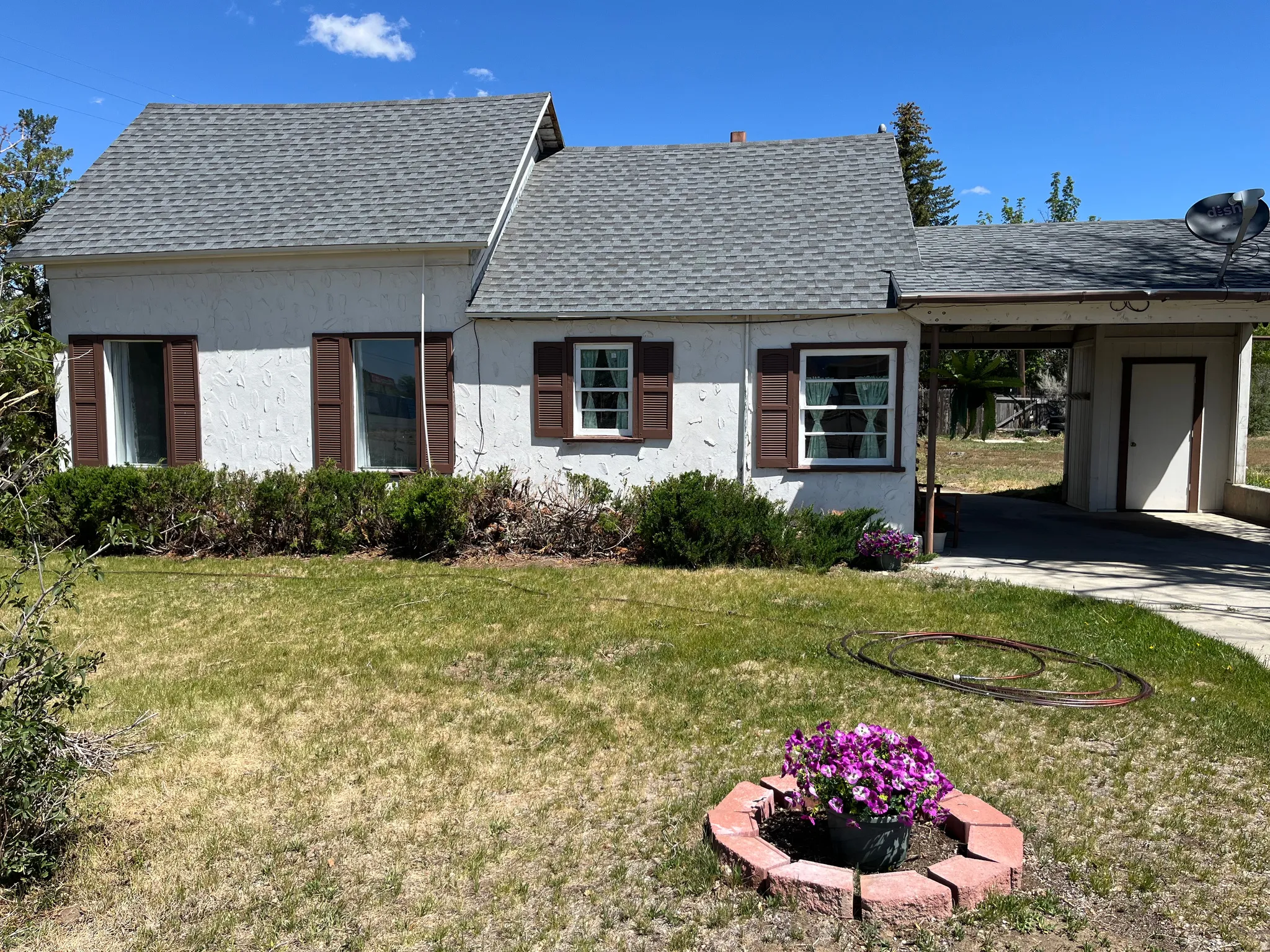 White stucco exterior with a gray shingle roof and brown window shutters