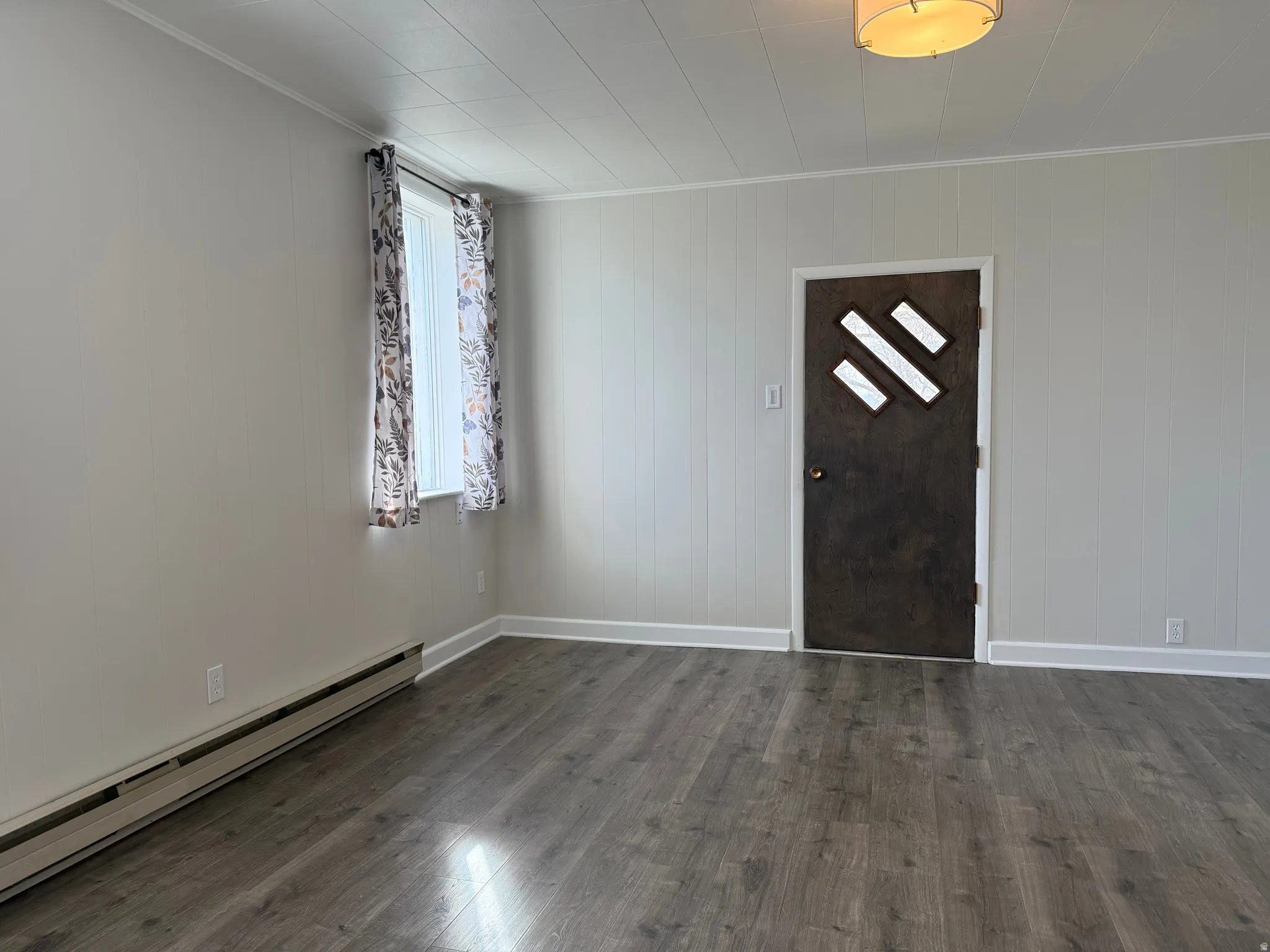 Entrance foyer featuring a baseboard radiator, dark wood finished floors, wooden walls, and ornamental molding