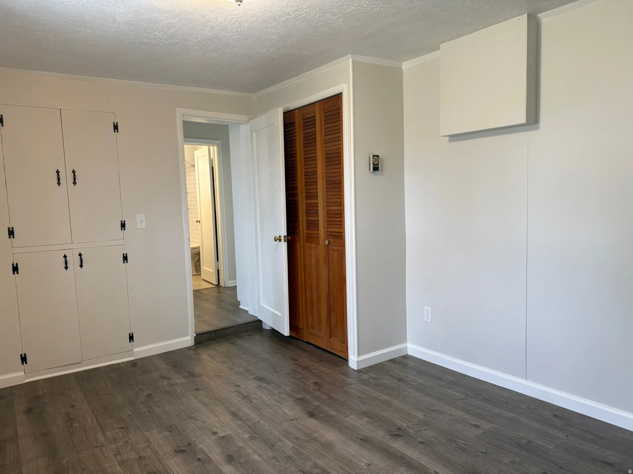 Unfurnished bedroom featuring a textured ceiling, dark wood-type flooring, and a closet