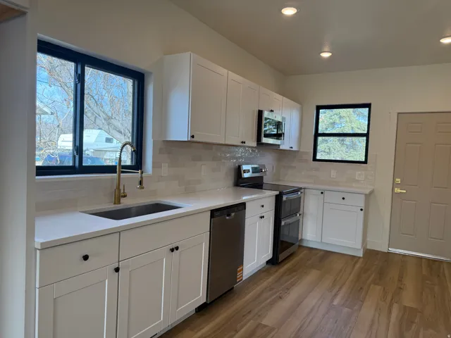 Kitchen featuring white cabinetry, stainless steel appliances, decorative backsplash, dark wood finished floors, and light stone counters
