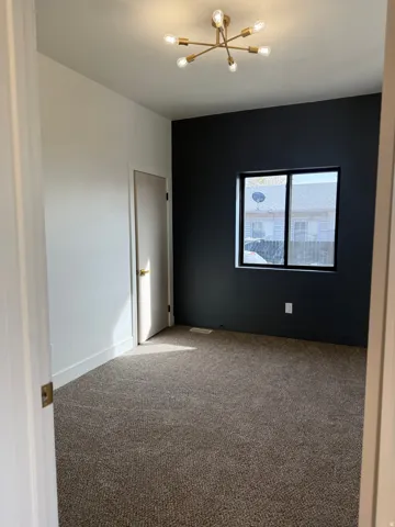 Carpeted empty room featuring baseboards and a chandelier