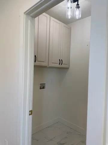 Laundry area featuring cabinet space, hookup for a washing machine, and light marble finish floors