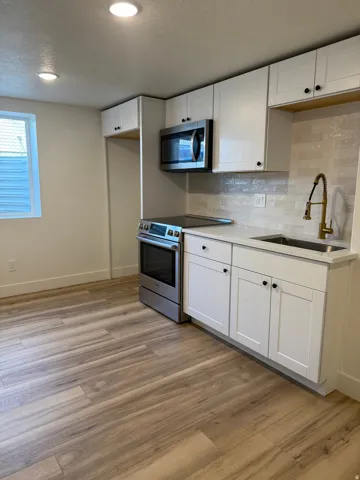 Kitchen with stainless steel appliances, white cabinetry, a textured ceiling, backsplash, and light wood finished floors