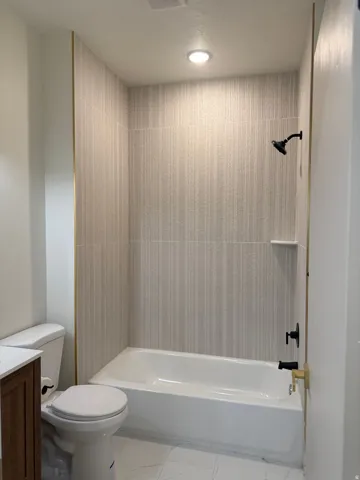 Full bath featuring vanity, light marble finish flooring, and washtub / shower combination