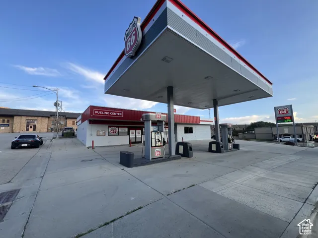 Commercial fueling station featuring a concrete canopy, multiple fuel dispensers, a paved lot, and a storefront structure
