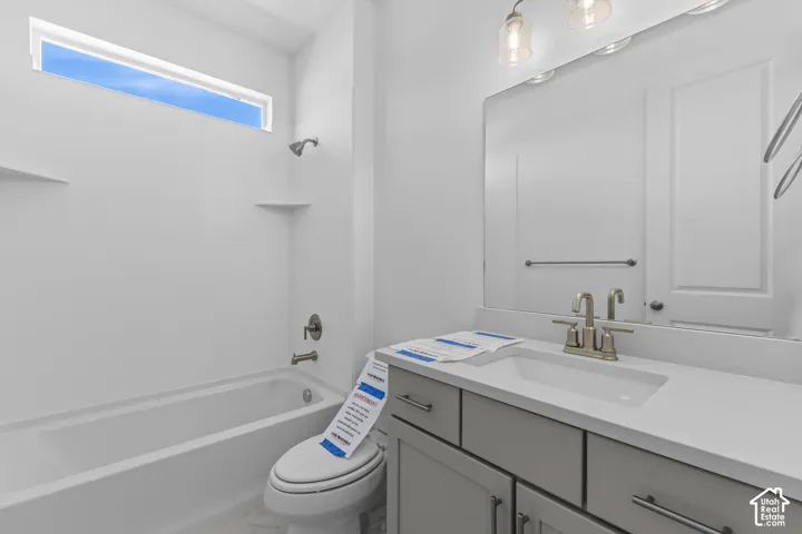 White vanity with a single basin sink and brushed nickel faucet, large vanity mirror with overhead lighting, white tub with shower head, and an elongated transom window