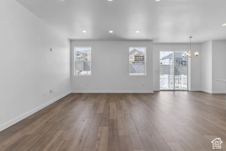 Spacious room featuring wood-finish flooring, recessed ceiling lights, multiple windows, and a sliding glass door
