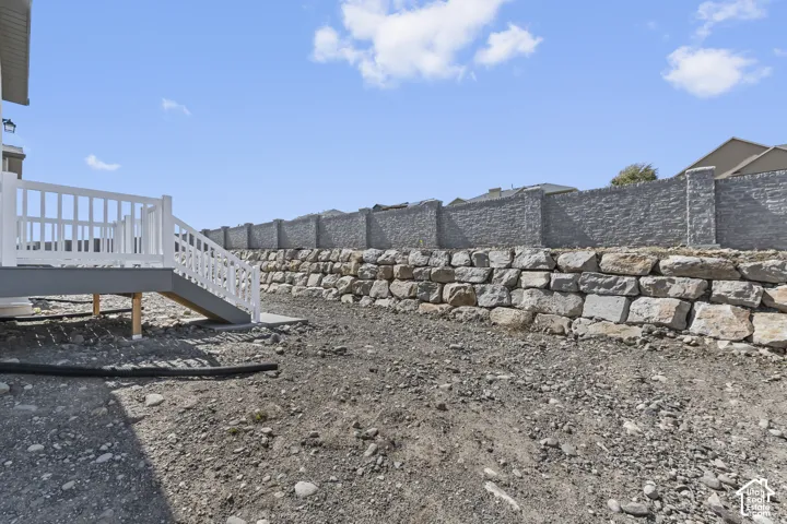 Elevated deck with white railing, stone retaining wall, and textured privacy wall