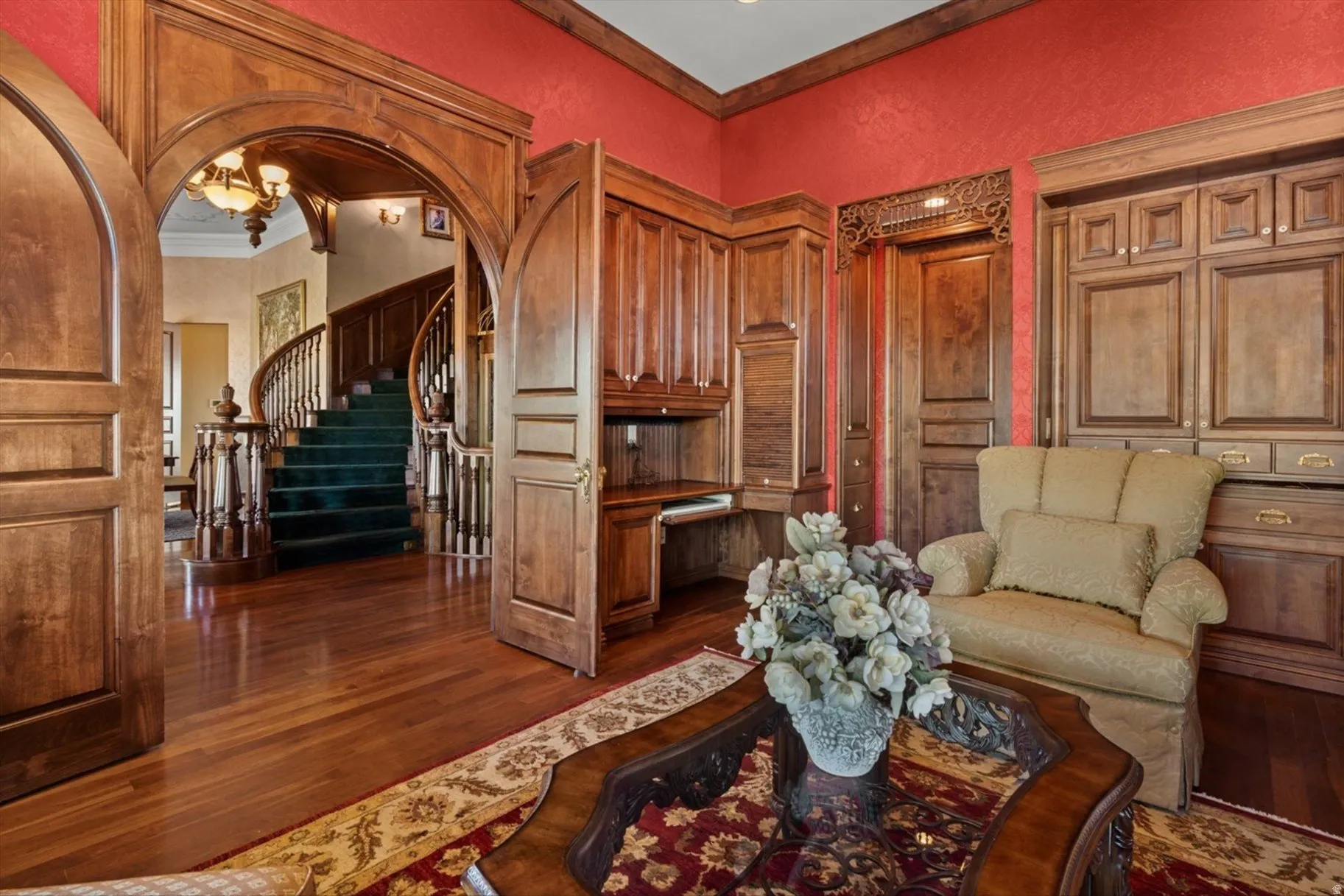 Hardwood flooring throughout, custom built-in cabinetry, arched doorways with intricate wood trim, and a grand curved staircase