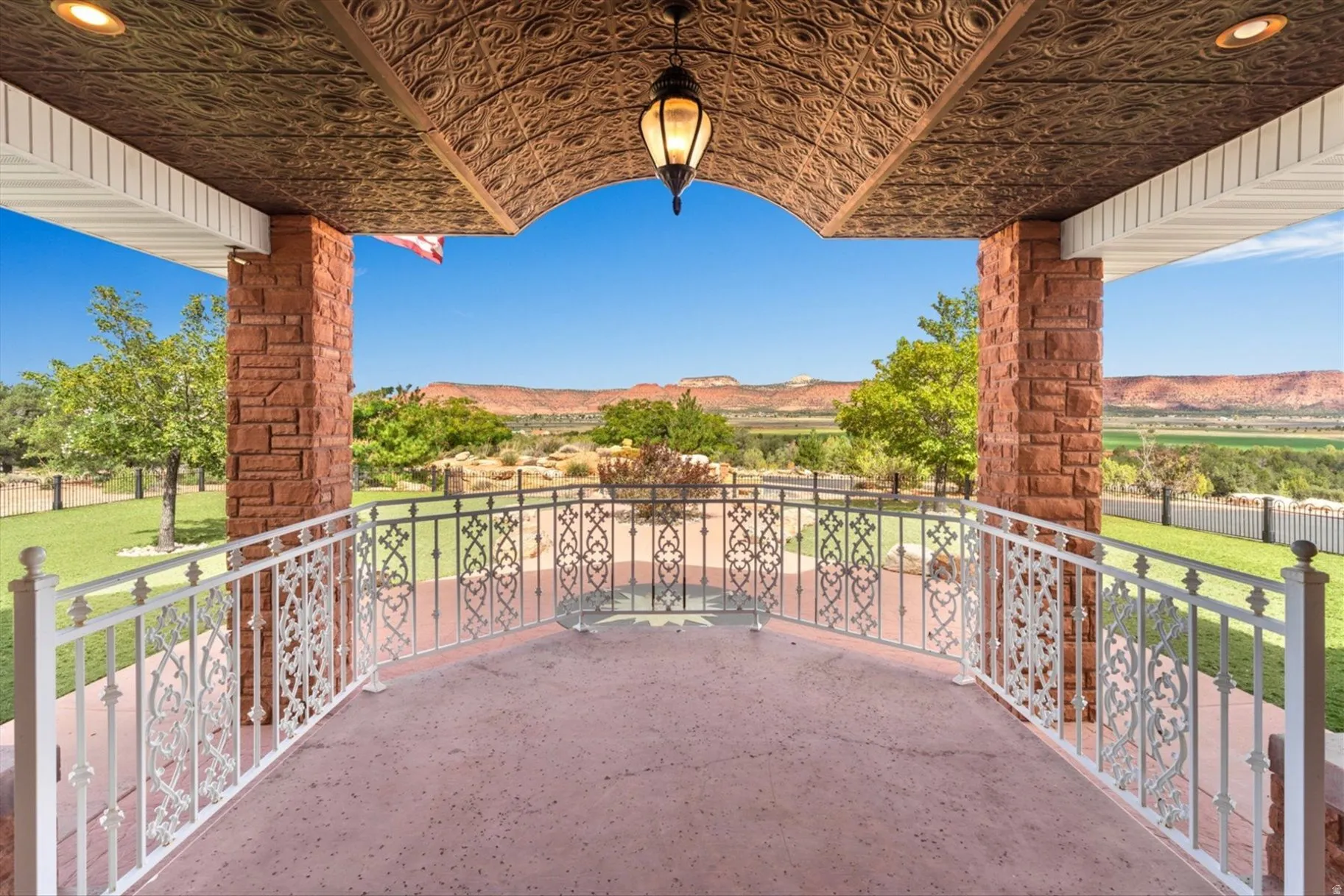 Covered patio featuring an ornate metal ceiling, stone-clad pillars, and decorative wrought iron railings