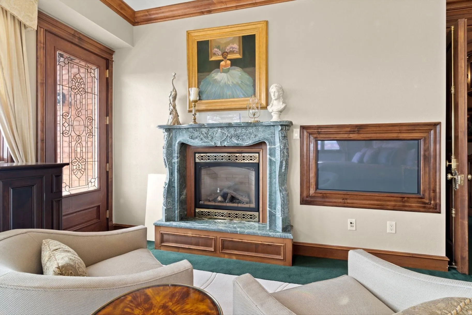 Decorative wood-framed glass entry door, ornamental fireplace with a stone surround, wood-paneled fireplace base, built-in wall-mounted display, and decorative crown molding