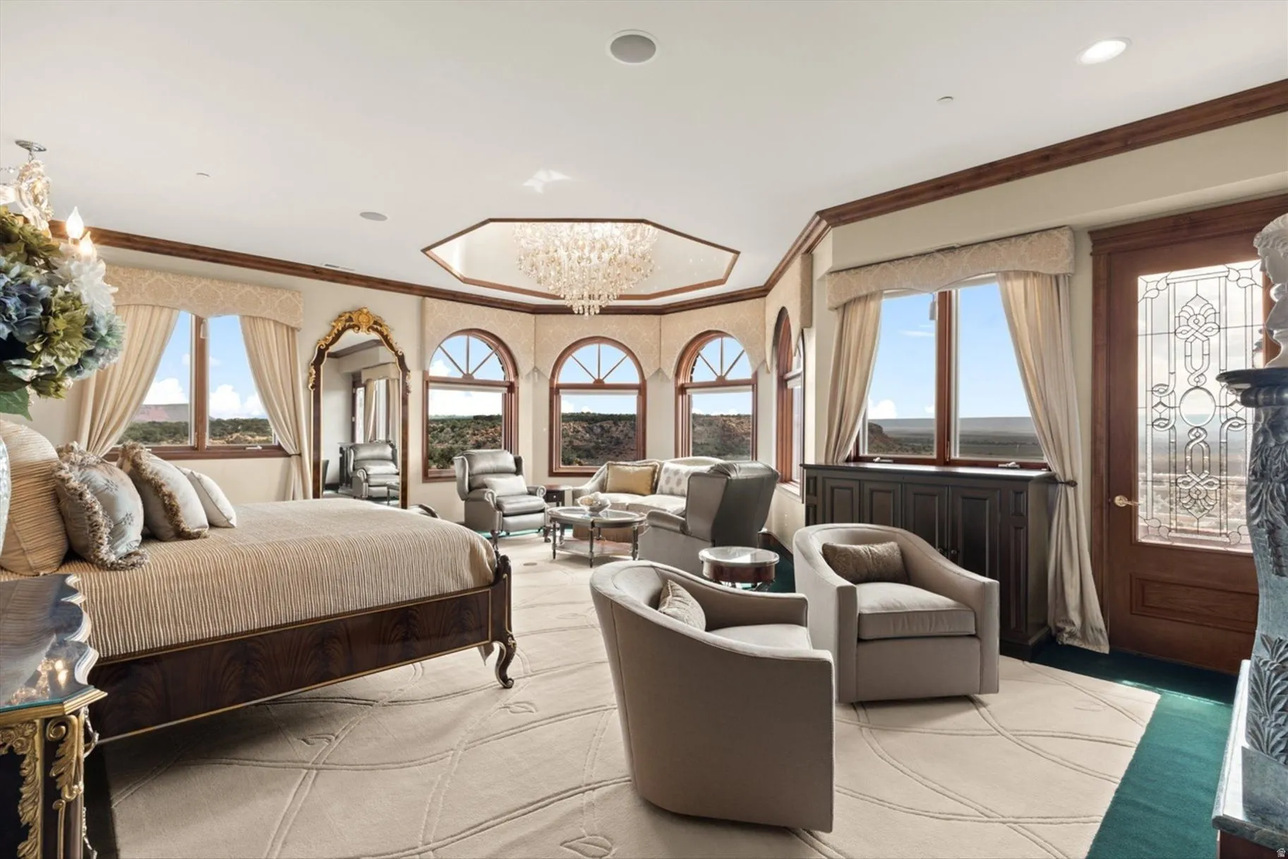 Spacious room with a decorative ceiling chandelier, multiple arched windows, and a wood-paneled door with an etched glass insert