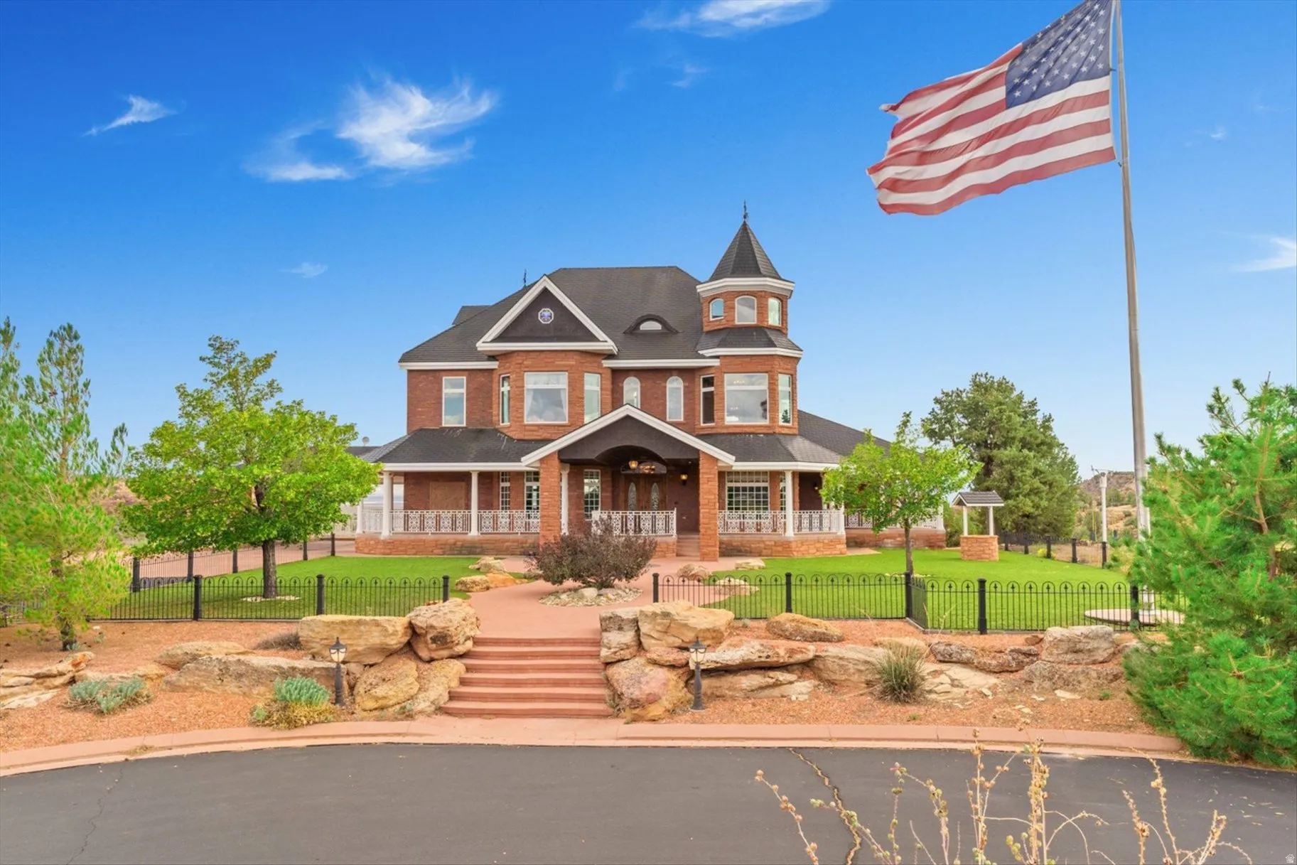 Brick exterior with turret, covered front porch, wrought iron fencing, and manicured lawn