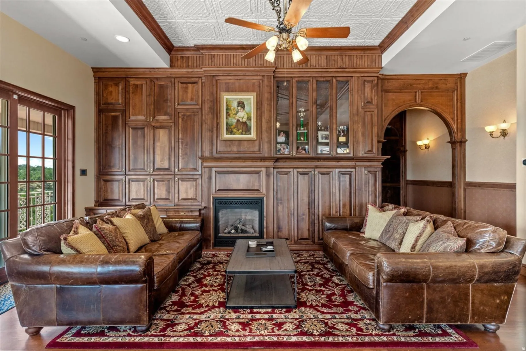 Expansive wood-paneled wall with integrated fireplace, glass-front cabinetry, and arched entryway