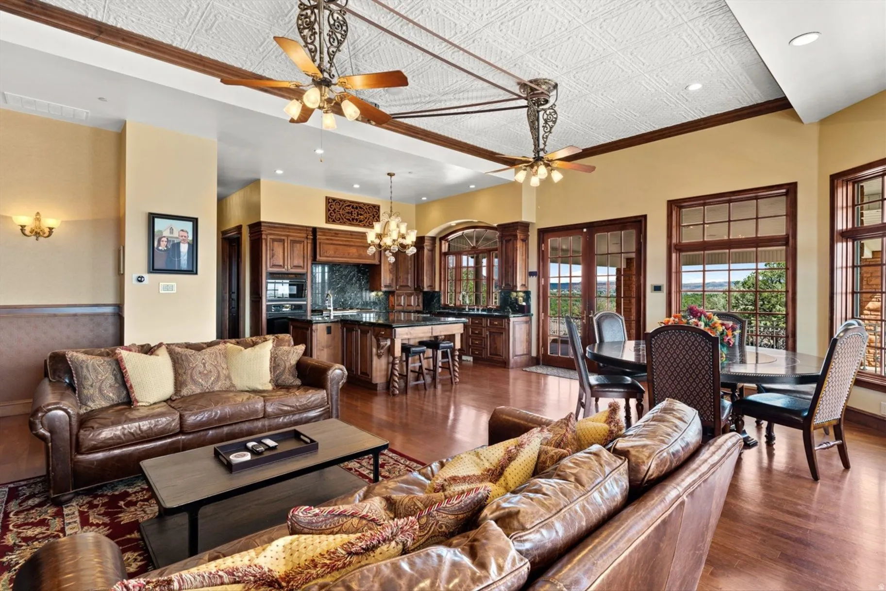 Wood-finish flooring throughout, kitchen with dark wood cabinetry and stone countertops, decorative ceiling fans, dining area with exterior access, and large windows with outdoor views