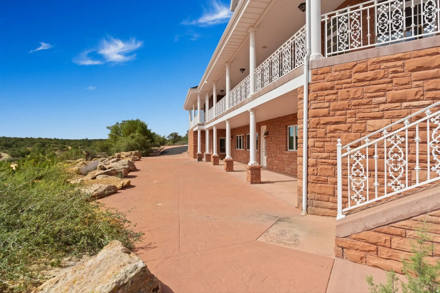 Stone veneer exterior with a covered lower patio and an upper-level balcony featuring decorative white railings
