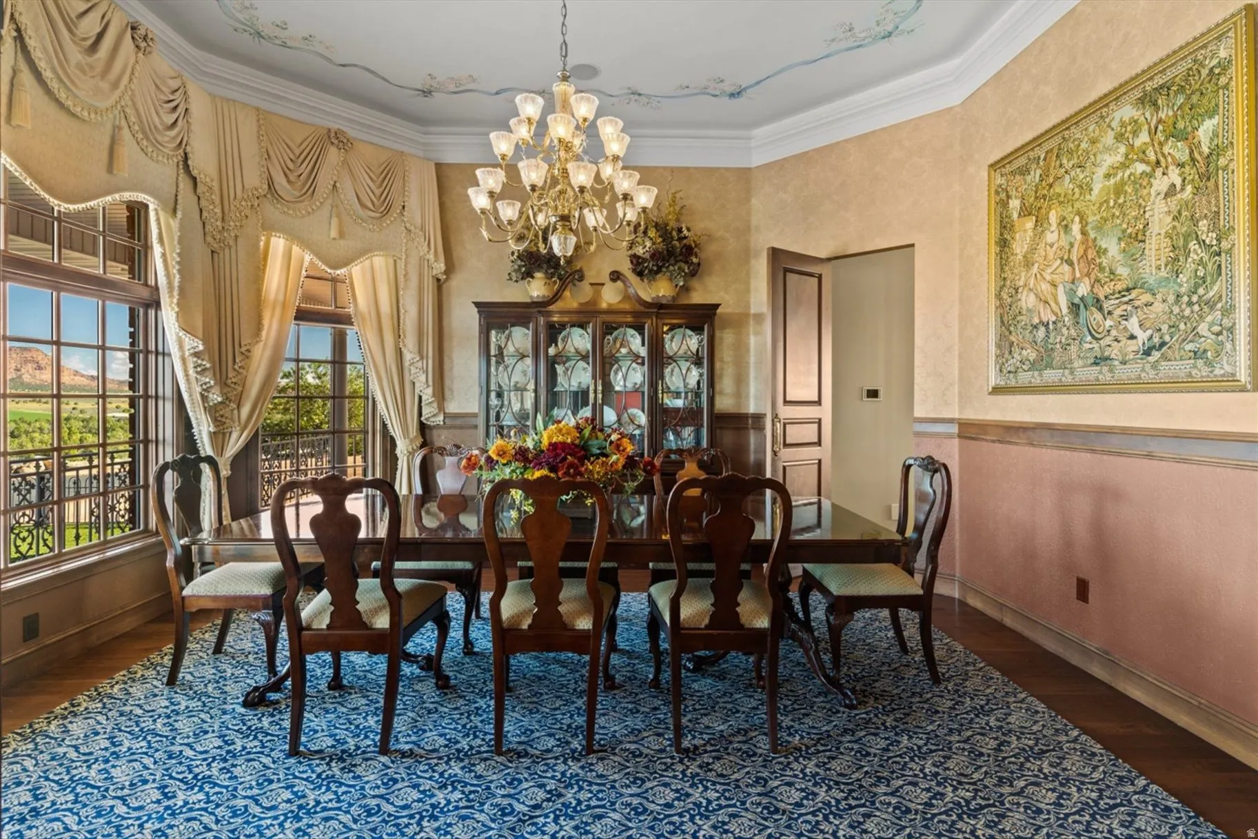 Wood-finish flooring with a decorative area rug, large picture windows, and a multi-tiered chandelier