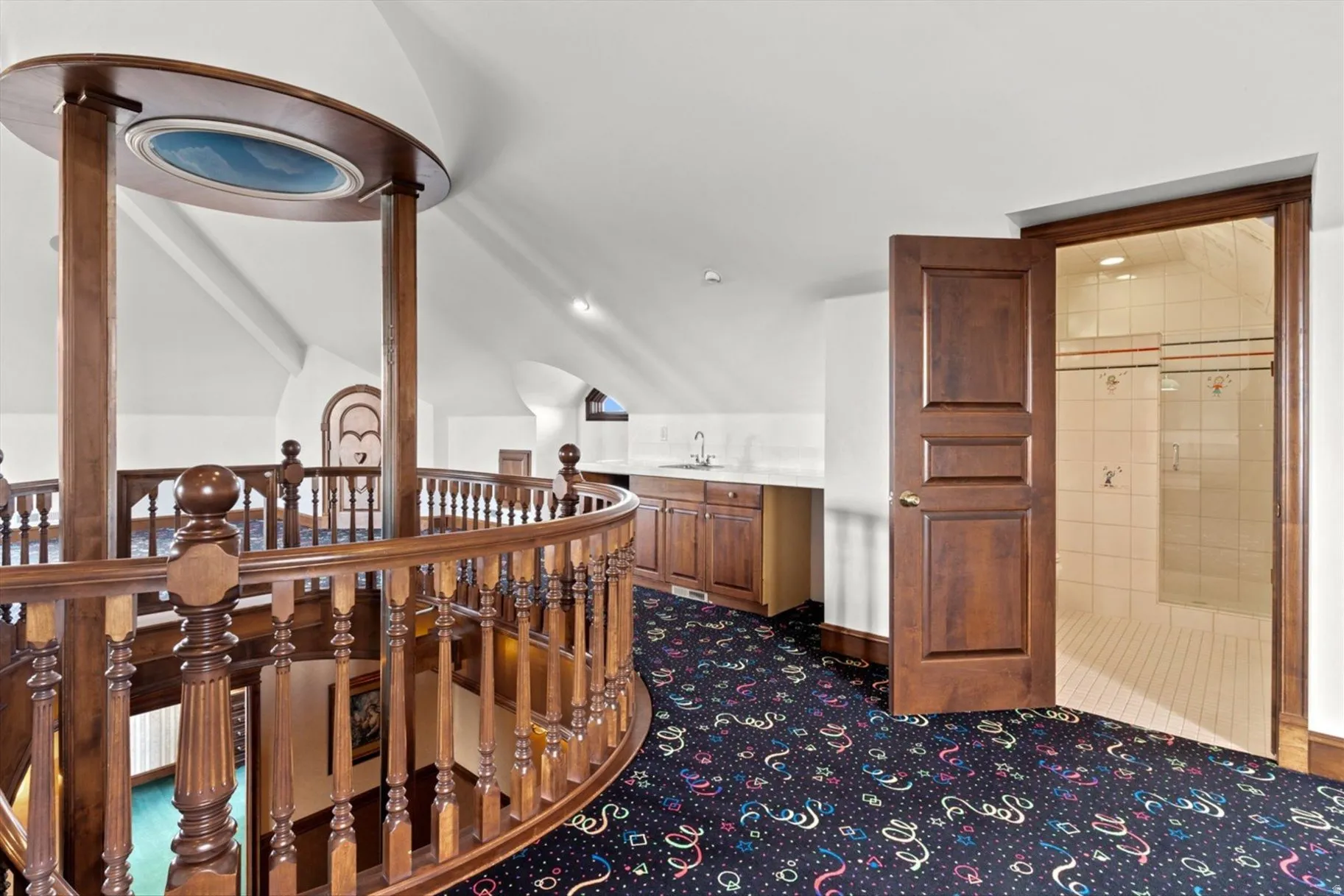 Curved wood balustrade overlooking a lower level, built-in wet bar with wood cabinetry, and a full bathroom featuring tile flooring and tiled shower walls