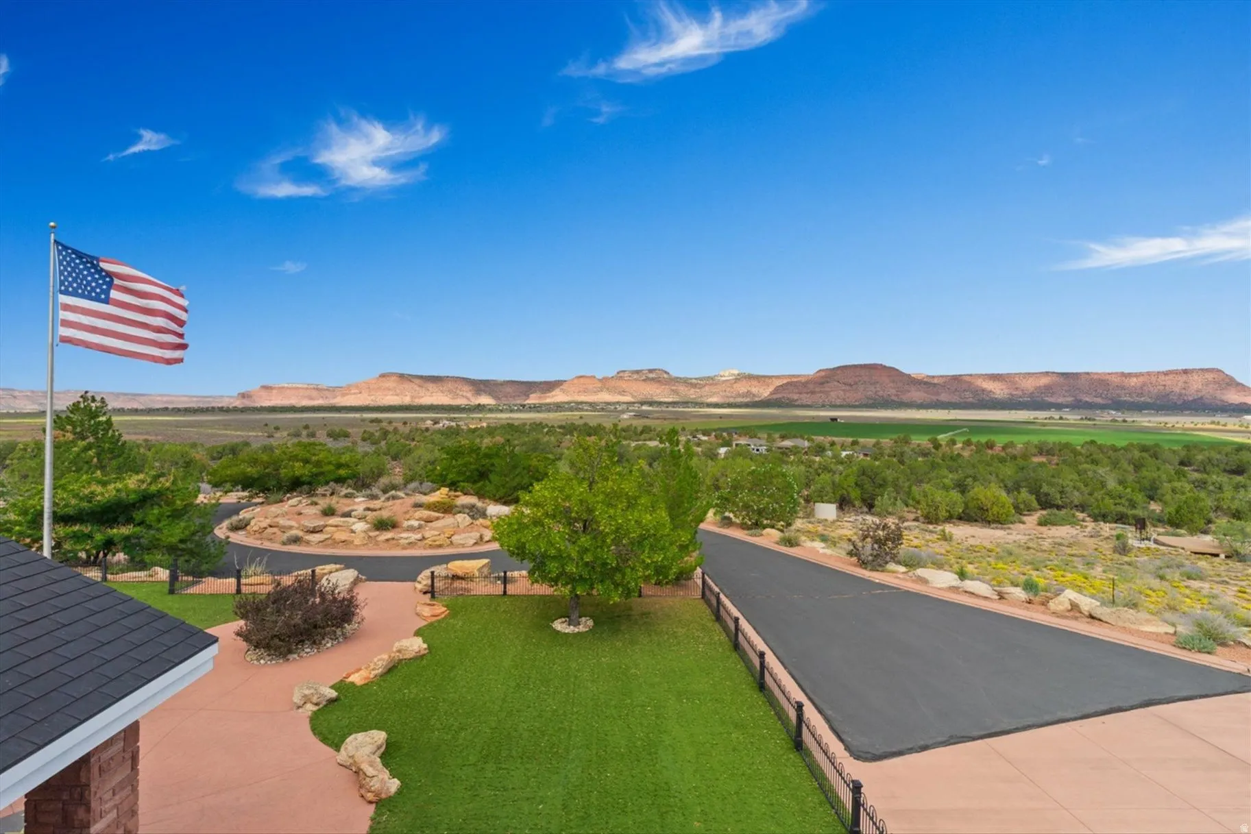 Expansive outdoor landscape featuring a paved circular drive, a sloped asphalt driveway, a red rock patio, and desert-style landscaping