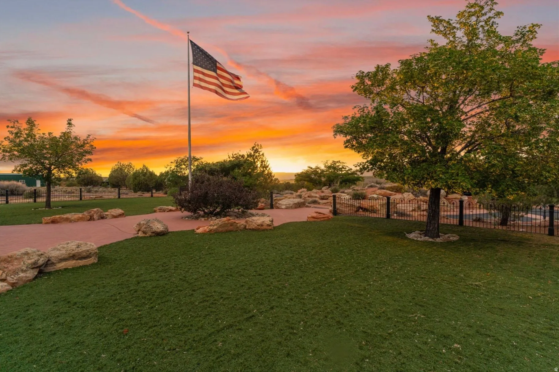 Manicured green space with mature trees, a paved pathway, and decorative rock landscaping