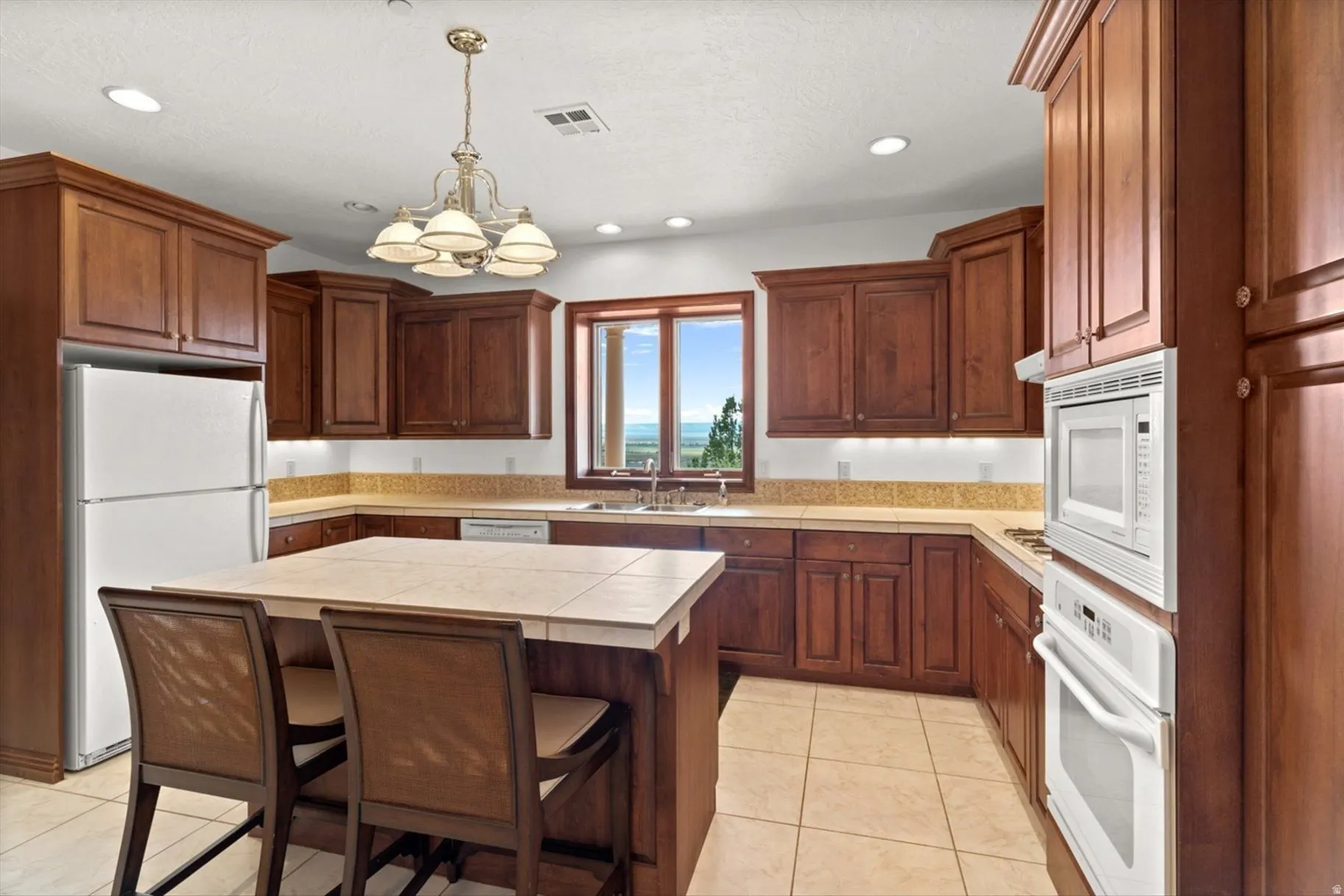 Kitchen featuring wood cabinetry, a center island with bar seating, tile flooring, and integrated white appliances