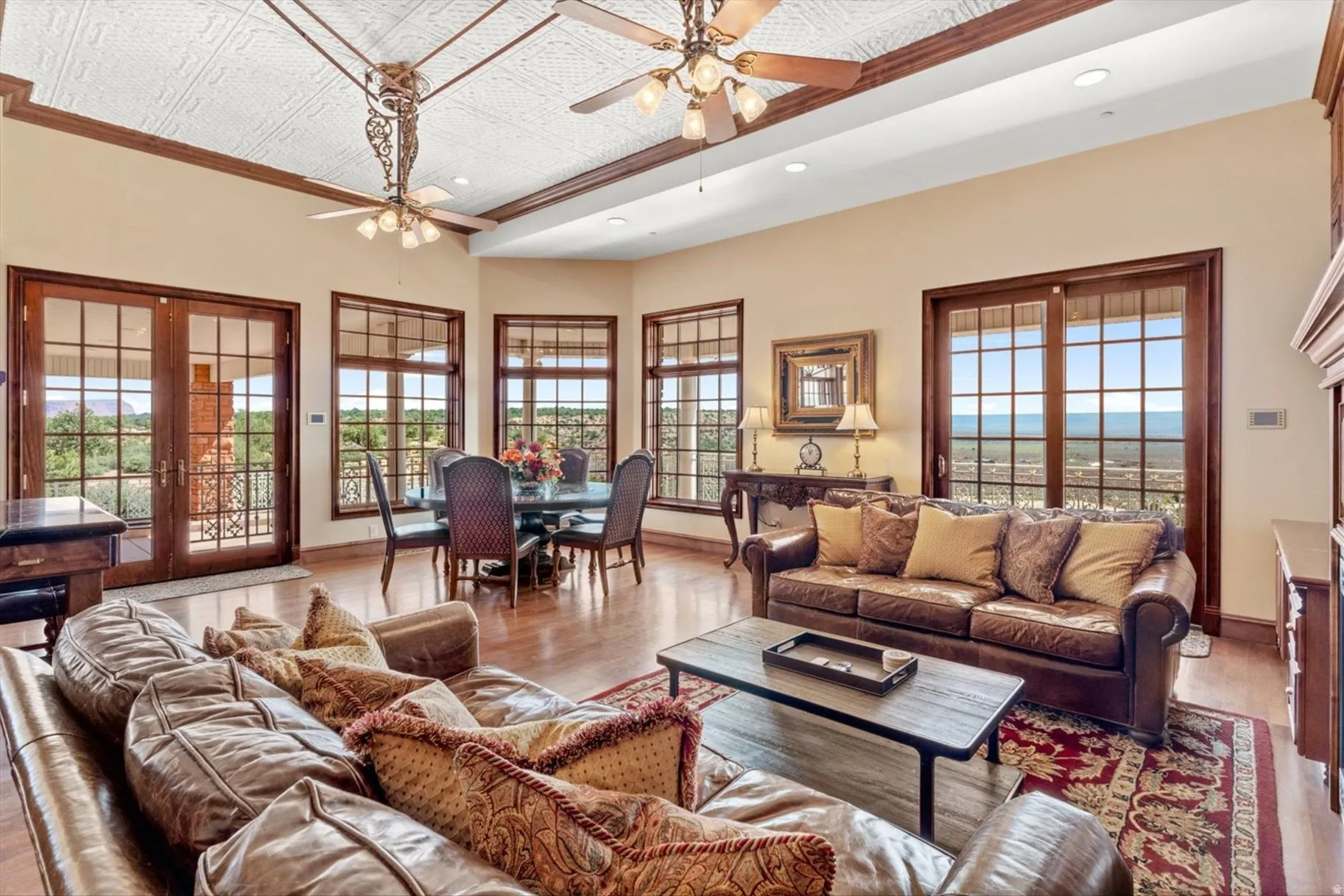 Hardwood flooring, coffered ceiling with decorative ceiling fans, wood-framed doors with glass panels, and multiple windows