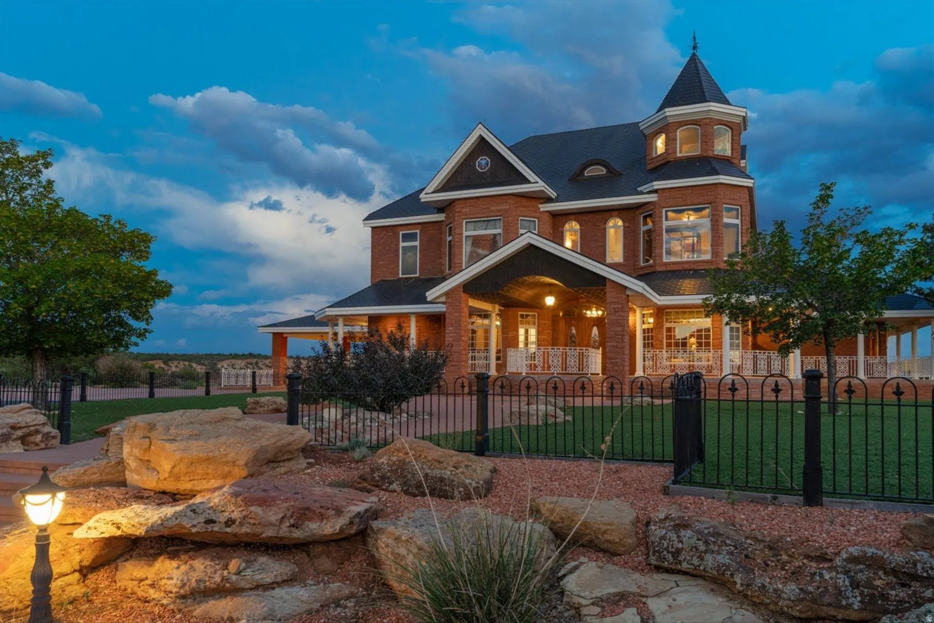 Brick exterior with a turret, covered front entry, wrap-around porch, and wrought iron fencing