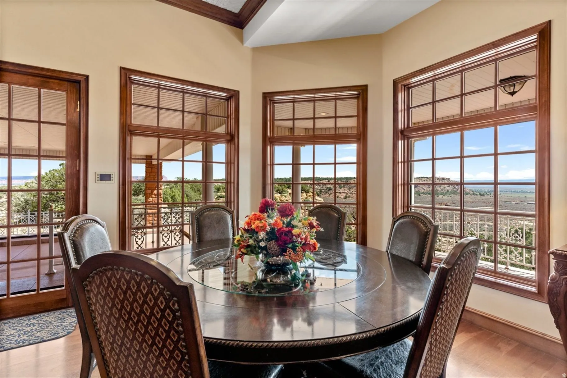 Wood-finish flooring with a circular dining table, surrounded by multiple windows with grid patterns, and a glass door leading to a patio