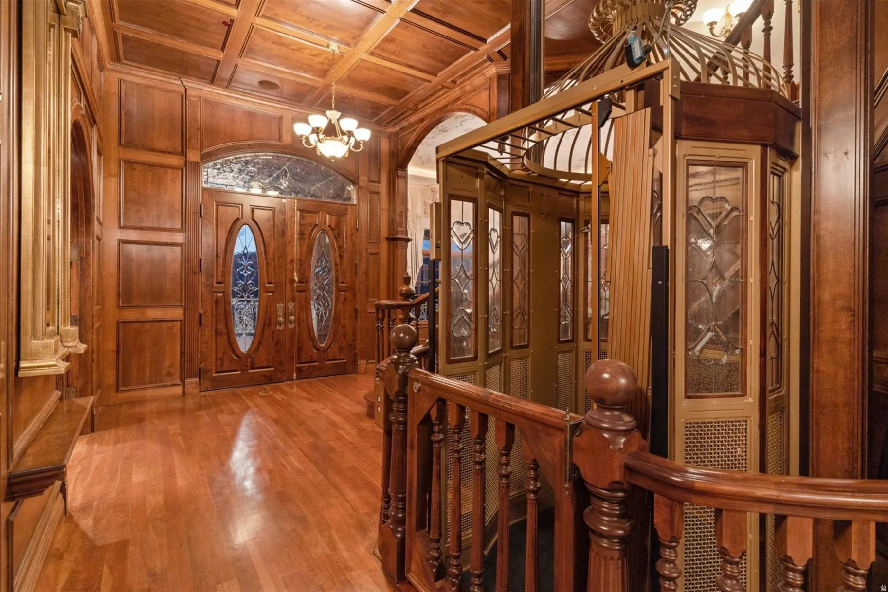 Grand foyer showcasing rich wood paneling throughout, coffered ceiling detail, and ornamental chandelier