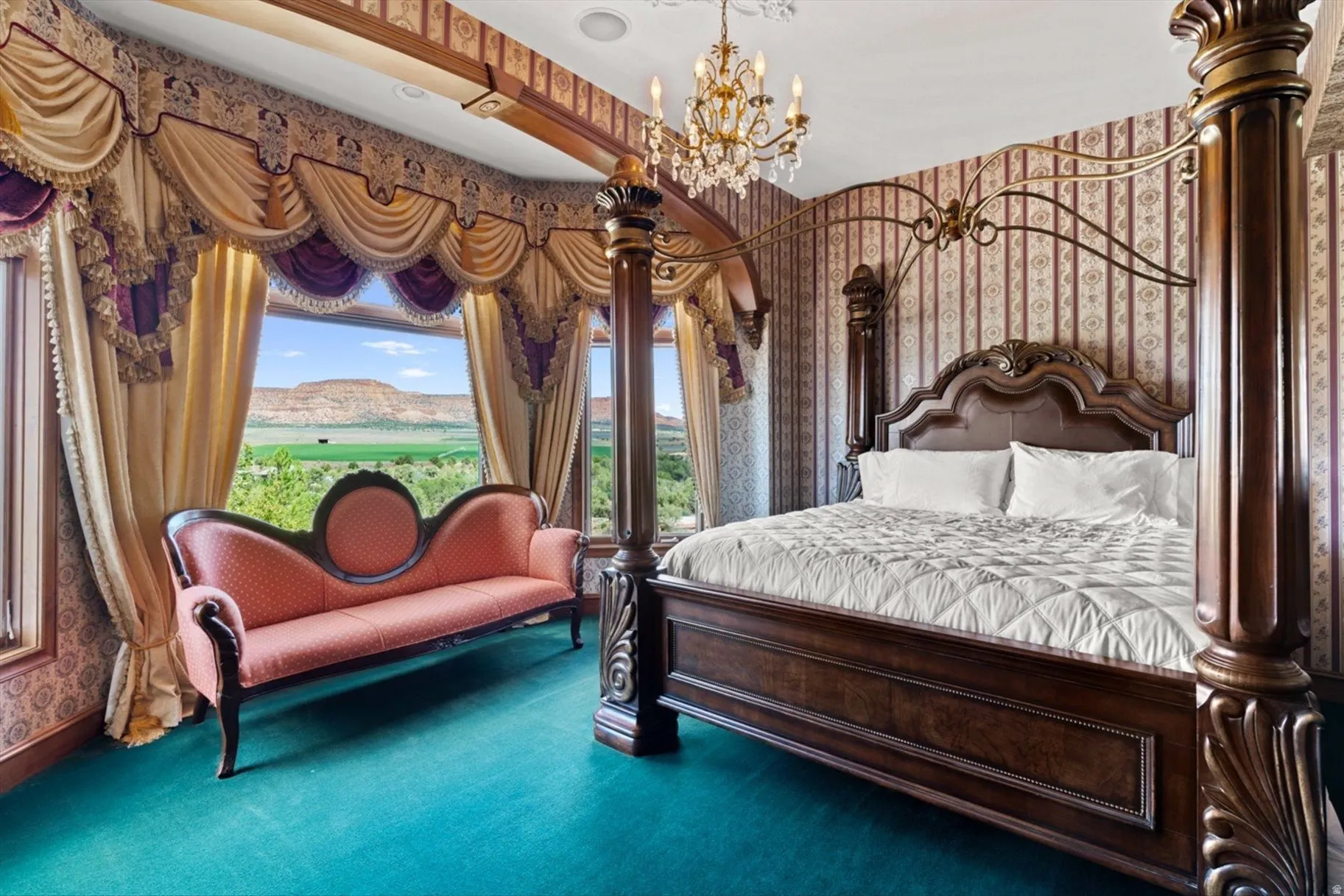 Large windows with custom drapery, ornate chandelier lighting, patterned wallpaper, and a dark wood four-poster bed frame